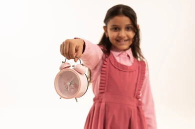 The concept of organizing and managing time, preparing for the new school year, education in Saudi Arabia, close-up portrait of a Saudi Arabian Gulf girl wearing a school uniform holding an alarm clock, white background.