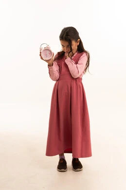 مفهوم تنظيم و إدارة الوقت, الاستعداد للعام الدراسي الجديد, التعليم في المملكة العربية السعودية, بورتريه لفتاة عربية خليجية سعودية ترتدي الزي المدرسي  تمسك بيدها ساعة المنبه, الجسم بالطول الكامل, خلفية بيضاء