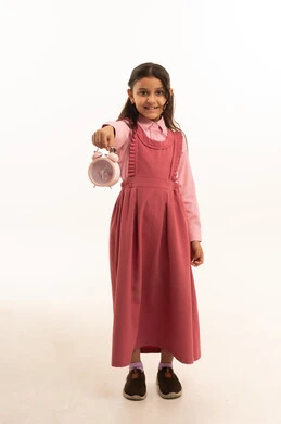 مفهوم تنظيم و إدارة الوقت, الاستعداد للعام الدراسي الجديد, التعليم في المملكة العربية السعودية, بورتريه لفتاة عربية خليجية سعودية ترتدي الزي المدرسي  تمسك بيدها ساعة المنبه, الجسم بالطول الكامل, خلفية بيضاء