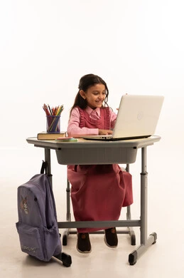 Use of modern technology, concept of distance learning, following online classes via the internet, portrait of a Saudi Arabian Gulf Arab female student wearing school uniform sitting at a study table working on a laptop with an expression of pleasure, white background