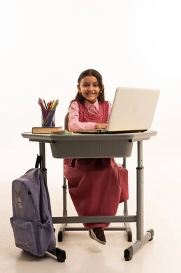 استخدام التكنولوجيا الحديثة، مفهوم التعلم عن بعد, متابعة حصص الاونلاين عن طريق الانترنت، بورتريه لطالبة عربية خليجية سعودية ترتدي اليونيفووم المدرسي تجلس على طاولة الدراسة   تعمل على جهاز الحاسوب المحمول بتعابير السرور، خلفية بيضاء