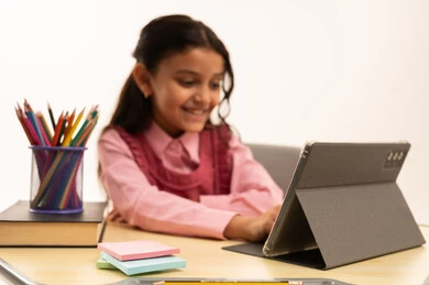 مفهوم التعلم عن بعد, متابعة حصص الاونلاين عن طريق الانترنت, استخدام التكنولوجيا الحديثة، بورتريه لطالبة عربية خليجية سعودية ترتدي اليونيفووم المدرسي تجلس على طاولة الدراسة   تعمل على جهاز التابلت اللوحي بتعابير السرور، خلفية بيضاء