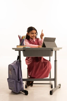 متابعة حصص الاونلاين عن طريق الانترنت, استخدام التكنولوجيا الحديثة، مفهوم التعلم عن بعد، بورتريه لطالبة عربية خليجية سعودية ترتدي اليونيفووم المدرسي تجلس على طاولة الدراسة   تعمل على جهاز التابلت اللوحي بتعابير السرور، خلفية بيضاء