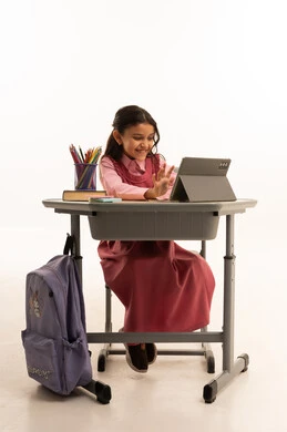 متابعة حصص الاونلاين عن طريق الانترنت, استخدام التكنولوجيا الحديثة، مفهوم التعلم عن بعد، بورتريه لطالبة عربية خليجية سعودية ترتدي اليونيفووم المدرسي تجلس على طاولة الدراسة   تعمل على جهاز التابلت اللوحي بتعابير السرور، خلفية بيضاء