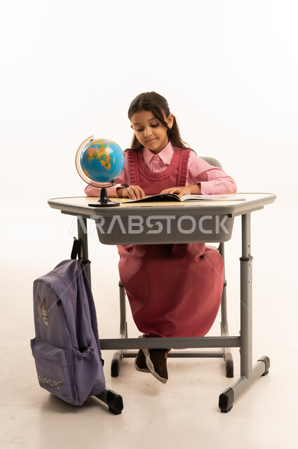 أهمية التعليم في بناء مستقبل مشرق للمجتمع ، مفهوم البحث والإستكشاف حول العالم، بورتريه لطالبة عربية خليجية سعودية ترتدي الزي المدرسي تجلس على طاوله مكتبية تقوم بمذاكره الدروس المدرسيه، خلفية بيضاء