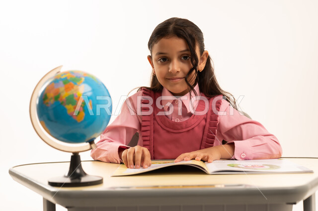 أهمية التعليم في بناء مستقبل مشرق للمجتمع ، مفهوم البحث والإستكشاف حول العالم، بورتريه لطالبة عربية خليجية سعودية ترتدي الزي المدرسي تجلس على طاوله مكتبية تقوم بمذاكره الدروس المدرسيه، خلفية بيضاء