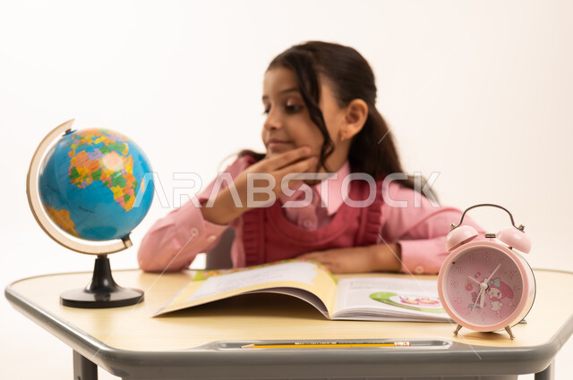 The importance of education in building a bright future for society, the concept of research and exploration around the world, a portrait of a Saudi Arabian Gulf student wearing a school uniform sitting at an office table studying school lessons, white background