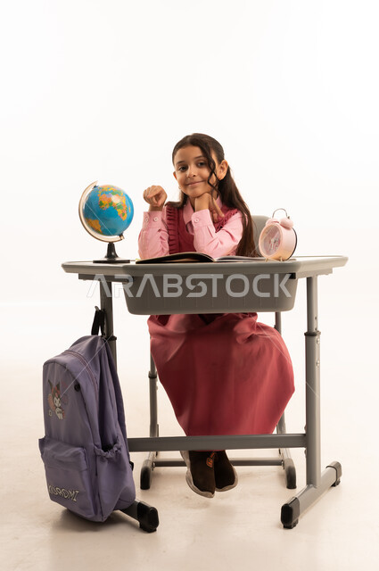 أهمية التعليم في بناء مستقبل مشرق للمجتمع ، مفهوم البحث والإستكشاف حول العالم، بورتريه لطالبة عربية خليجية سعودية ترتدي الزي المدرسي تجلس على طاوله مكتبية تقوم بمذاكره الدروس المدرسيه، خلفية بيضاء