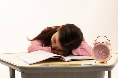 Sleeping on the study table, gestures of drowsiness, fatigue and exhaustion, portrait of a Saudi Arabian Gulf Arab student wearing a school uniform neglecting her lessons, negatives of distance learning, wasting time, white background