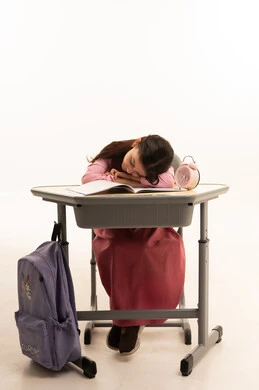 النوم على طاولة الدراسة، ايماءات النعاس والتعب والإرهاق، بورتريه لطالبة عربية خليجية سعودية ترتدي اليونيفورم المدرسي تقوم بإهمال دروسها، سلبيات التعلم عن بعد، هدر وضياع الوقت، خلفية بيضاء