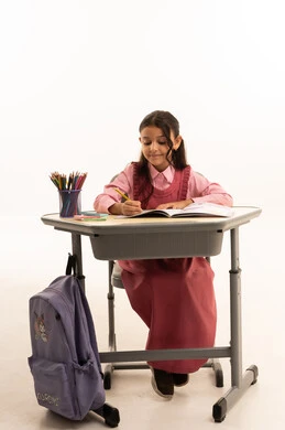 مفهوم العودة إلى المدارس، مراجعة الدروس اليومية, التعليم في المملكة العربية السعودية, الاستعداد للعام الدراسي الجديد, بورتريه لفتاة عربية خليجية سعودية ترتدي الزي المدرسي تجلس على الطاولة المكتبية تقوم بالكتابة فى الدفتر, خلفية بيضاء