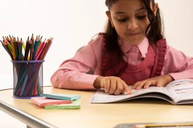 مراجعة الدروس اليومية, مفهوم العودة إلى المدارس، التعليم في المملكة العربية السعودية, الاستعداد للعام الدراسي الجديد, بورتريه مقرب لفتاة عربية خليجية سعودية ترتدي الزي المدرسي تجلس على الطاولة المكتبية تقوم بالكتابة فى الدفتر, خلفية بيضاء