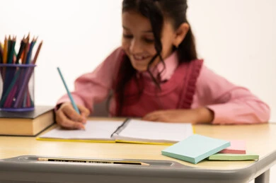 Reviewing daily lessons, back to school concept, education in Saudi Arabia, preparing for the new school year, close-up portrait of a Saudi Arabian Gulf girl wearing school uniform sitting at an office table writing in a notebook, white background