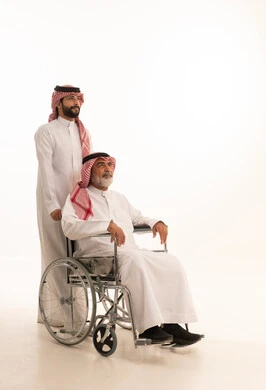  العنايه بأصحاب الهمم وتأمين احتياجاتهم، توفير اجهزة ومعدات تساعد بالتنقل، بورتريه  لرجل عربي سعودي خليجي يرتدي الشماغ والثوب التقليدي يقوم بمساعدة ابيه من ذوي الاحتياجات الخاصه يجلس على كرسي متحرك، شعور المعاقين بالإنتماء والتقدير والإحترام في السعوديه، خلفيه بيضاء