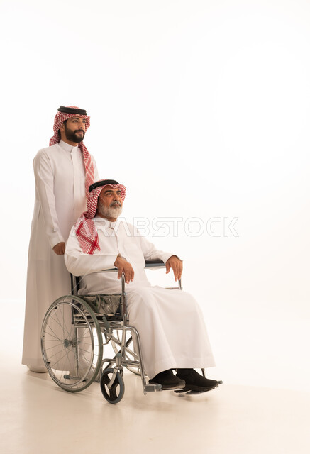 توفير اجهزة ومعدات تساعد بالتنقل، العنايه بأصحاب الهمم وتأمين احتياجاتهم، بورتريه  لرجل عربي سعودي خليجي يرتدي الشماغ والثوب التقليدي يقوم بمساعدة ابيه من ذوي الاحتياجات الخاصه يجلس على كرسي متحرك، شعور المعاقين بالإنتماء والتقدير والإحترام في السعوديه، خلفيه بيضاء
