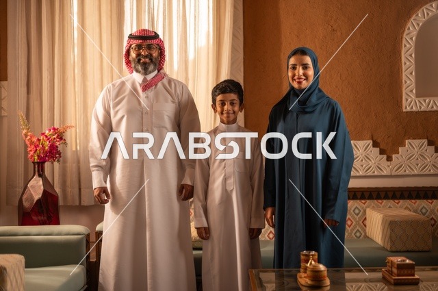 تفاصيل المكان المزخرف مع لمسات ديكور ومزهرية تحتوي على ورود ملونة، دعم الأولاد من قبل الأبوين، إظهار مشاعر المودة والمحبة العائلية, عائلة عربية خليجية سعودية تقف داخل غرفة تراثية بديكورات جدران عصرية, تفاصيل المكان المزخرف مع لمسات ديكور تراثية عربية