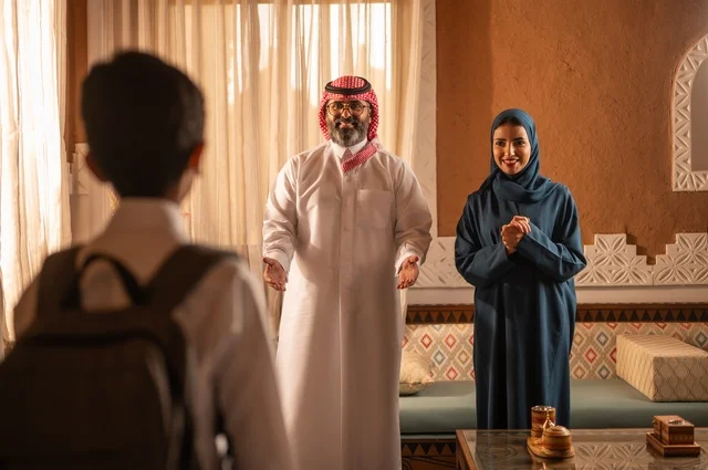 وقت العودة من المدرسة، إظهار مشاعر المودة والمحبة العائلية, عائلة عربية خليجية سعودية تقف داخل غرفة تراثية بديكورات جدران مزخرفة,  في الخلفية تفاصيل المكان المزخرف مع لمسات ديكور تراثية عربية