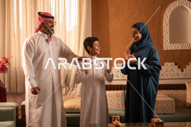 ألعاب الأصابع تضيف جوا من المتعة والتسلية، إظهار مشاعر المودة والمحبة العائلية, عائلة عربية خليجية سعودية تقف داخل غرفة تراثية بديكورات جدران عصرية، تفاصيل المكان المزخرف مع لمسات ديكور تراثية عربية ومزهرية تحتوي على ورود ملونة، التسلية في وقت الفراغ