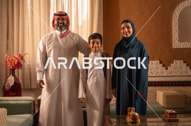 التقاط صورة عائلية بعد العودة من المدرسة، دعم الأولاد من قبل الأبوين، إظهار مشاعر المودة والمحبة العائلية, عائلة عربية خليجية سعودية تقف داخل غرفة تراثية بديكورات جدران مزخرفة,  في الخلفية تفاصيل المكان المزخرف مع لمسات ديكور تراثية عربية