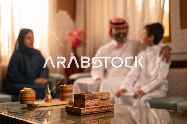 التفاهم والانسجام بين أفراد الأسرة مع الكبير والصغير، إظهار مشاعر المودة والمحبة العائلية, عائلة عربية خليجية سعودية تجلس داخل غرفة تراثية بديكورات جدران مزخرفة,  في الخلفية تفاصيل المكان المزخرف مع لمسات ديكور تراثية عربية
