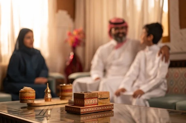 التفاهم والانسجام بين أفراد الأسرة مع الكبير والصغير، إظهار مشاعر المودة والمحبة العائلية, عائلة عربية خليجية سعودية تجلس داخل غرفة تراثية بديكورات جدران مزخرفة,  في الخلفية تفاصيل المكان المزخرف مع لمسات ديكور تراثية عربية