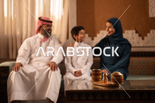 تبادل الأحاديث والمواقف المضجكة مع العائلة ، إظهار مشاعر المودة والمحبة العائلية,صورة لعائلة عربية خليجية سعودية تجلس داخل غرفة تراثية بديكورات جدران مزخرفة,  في الخلفية تفاصيل المكان المزخرف مع لمسات ديكور تراثية عربية، قضاء  وقت العطلة معا