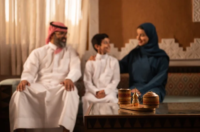 تبادل الأحاديث والمواقف المضجكة مع العائلة ، إظهار مشاعر المودة والمحبة العائلية,صورة لعائلة عربية خليجية سعودية تجلس داخل غرفة تراثية بديكورات جدران مزخرفة,  في الخلفية تفاصيل المكان المزخرف مع لمسات ديكور تراثية عربية، قضاء  وقت العطلة معا