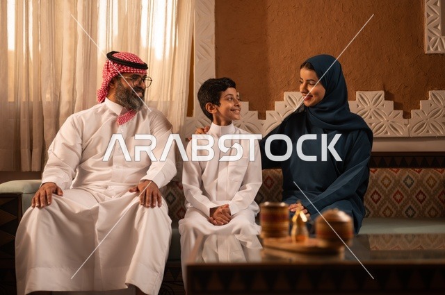التفاهم والانسجام بين أفراد الأسرة مع الكبير والصغير، إظهار مشاعر المودة والمحبة العائلية, عائلة عربية خليجية سعودية تجلس داخل غرفة تراثية بديكورات جدران مزخرفة,  في الخلفية تفاصيل المكان المزخرف مع لمسات ديكور تراثية عربية