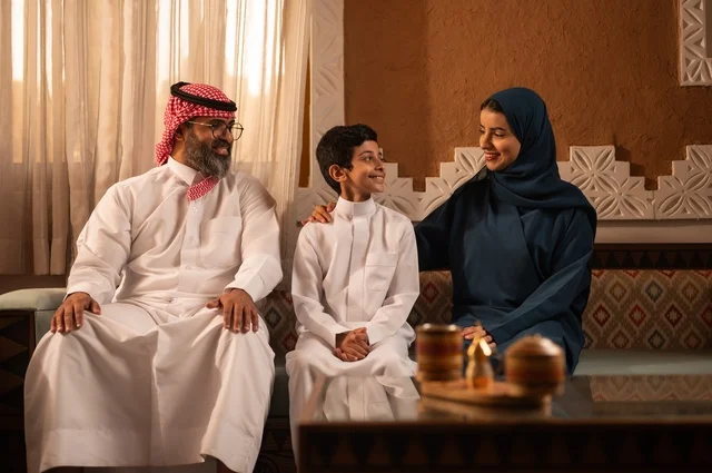 التفاهم والانسجام بين أفراد الأسرة مع الكبير والصغير، إظهار مشاعر المودة والمحبة العائلية, عائلة عربية خليجية سعودية تجلس داخل غرفة تراثية بديكورات جدران مزخرفة,  في الخلفية تفاصيل المكان المزخرف مع لمسات ديكور تراثية عربية