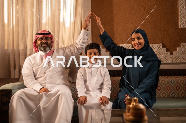 التفاهم بين الأبوين ينتج سعادة الأولاد، إظهار مشاعر المودة والمحبة العائلية, عائلة عربية خليجية سعودية تجلس داخل غرفة تراثية بديكورات جدران مزخرفة,  في الخلفية تفاصيل المكان المزخرف مع لمسات ديكور تراثية عربية، قضاء وقت العطلة معا