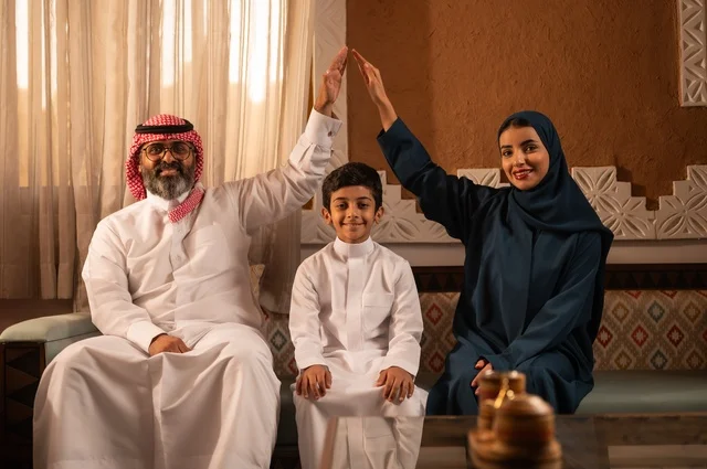التفاهم بين الأبوين ينتج سعادة الأولاد، إظهار مشاعر المودة والمحبة العائلية, عائلة عربية خليجية سعودية تجلس داخل غرفة تراثية بديكورات جدران مزخرفة,  في الخلفية تفاصيل المكان المزخرف مع لمسات ديكور تراثية عربية، قضاء وقت العطلة معا