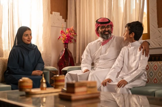 تبادل الأحاديث والمواقف المضجكة مع العائلة ، إظهار مشاعر المودة والمحبة العائلية,صورة لعائلة عربية خليجية سعودية تجلس داخل غرفة تراثية بديكورات جدران مزخرفة,  في الخلفية تفاصيل المكان المزخرف مع لمسات ديكور تراثية عربية، قضاء  وقت العطلة معا
