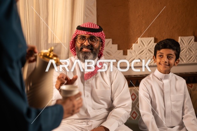 إظهار مشاعر المودة والمحبة العائلية, القهوة العربية تراث أصيل كرم الضيافة، تعليم العادات والتقاليد، صورة مق ربة لعائلة عربية خليجية سعودية تجلس داخل غرفة تراثية بديكورات جدران مزخرفة,  في الخلفية تفاصيل المكان المزخرف مع لمسات ديكور تراثية عربية