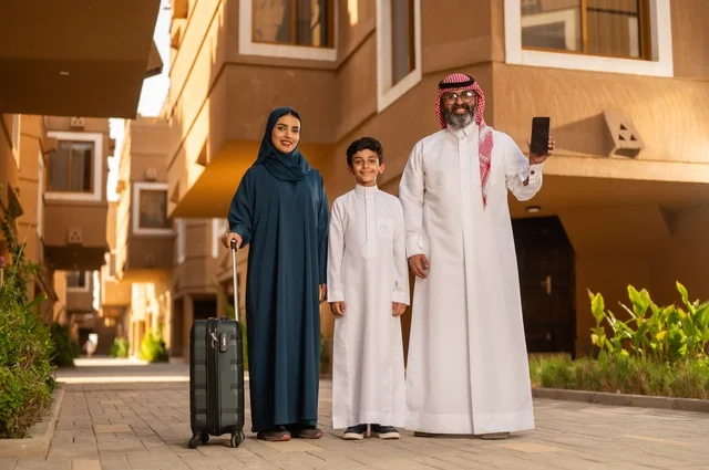 A black background displayed on a mobile phone, spending an entertaining summer trip, the atmosphere of the Gulf family and family bonding, a Saudi Arabian Gulf Arab family standing at the entrance of a modern home, the father wearing a white thobe with a ghutrah and agal, the child wearing a traditional white thobe, the mother holding a suitcase in her hand.