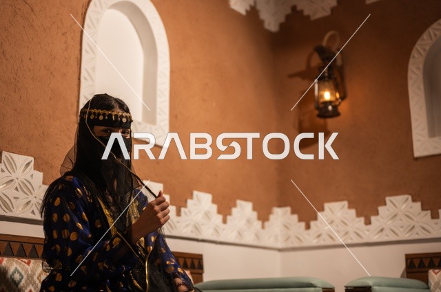 Pride in national identity, showing feelings of love and belonging to the homeland, a Saudi Arabian Gulf woman wearing a black abaya and burqa sitting in an old heritage house, the day of our beginnings in 1727 AD, the anniversary of the founding of the first Saudi state on February 22, wearing traditional folk costumes