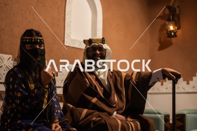 ارتداء الأزياء الشعبية التقليدي، إظهار مشاعر حب الوطن والانتماء إليه, الفخر بالهوية الوطنية, إمرأة عربية خليجية سعودية ترتدي العباءة السوداء والبرقع تجلس مع زوجها في بيت تراثي قديم, يوم بدينا 1727 م, ذكرى تأسيس الدولة السعودية الأولى في 22 فبراير