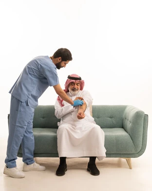 الاستعداد لأخذ الحقنة المسكنة للألم، مفهوم العمل في شركات التمريض المنزلي، تقديم أفضل الخدمات الطبية المنزلية للمرضى كبار السن، بورتريه لممرض يرتدي اللباس الطبي يقوم بإعطاء ابرة لرجل كبير بالسن عربي خليجي سعودي يرتدي الشماغ والثوب ويجلس على كنبه، خلفية بيضاء