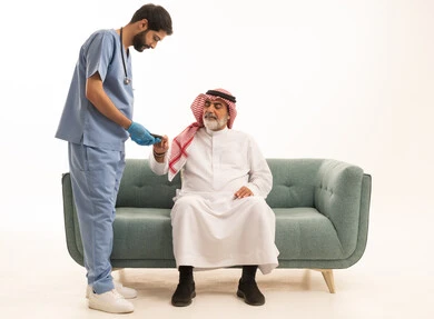 جهاز قياس سكر الدم لمرضى السكري، العمل في القطاع الطبي وشركات التمريض المنزلي، الرعاية الصحية والفحص الطبي السريع، بورتريه لممرض يرتدي المعطف الطبي يقوم بفحص نسبة السكر في الدم لمريض مسن عربي خليجي سعودي يرتدي الشماغ والثوب التقليدي يجلس على الكنبه، خلفية بيضاء