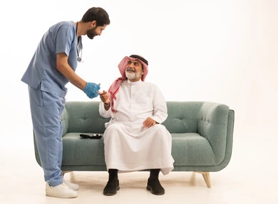 جهاز قياس سكر الدم لمرضى السكري، العمل في القطاع الطبي وشركات التمريض المنزلي، الرعاية الصحية والفحص الطبي السريع، بورتريه لممرض يرتدي المعطف الطبي يقوم بفحص نسبة السكر في الدم لمريض مسن عربي خليجي سعودي يرتدي الشماغ والثوب التقليدي يجلس على الكنبه، خلفية بيضاء