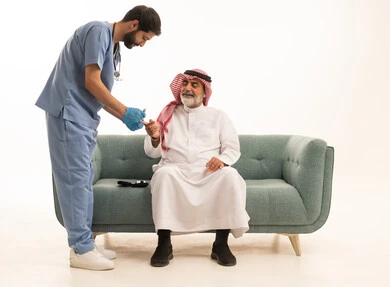 جهاز قياس سكر الدم لمرضى السكري، العمل في القطاع الطبي وشركات التمريض المنزلي، الرعاية الصحية والفحص الطبي السريع، بورتريه لممرض يرتدي المعطف الطبي يقوم بفحص نسبة السكر في الدم لمريض مسن عربي خليجي سعودي يرتدي الشماغ والثوب التقليدي يجلس على الكنبه، خلفية بيضاء