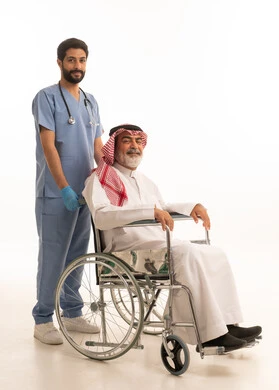 مفهوم الرعاية الصحية والاعتناء بالمرضى والمقعدين، نمط حياة ذوي الهمم، ايماءات السرور والسعادة، بورتريه لممرض يرتدي اليونيفورم والكمامة يقوم بالاعتناء برجل عربي خليجي سعودي مقعد يرتدي الثوب التقليدي والشماغ يجلس على كرسي متحرك، صورة لكامل الجسم، خلفية بيضاء