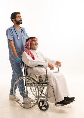 مفهوم الرعاية الصحية والاعتناء بالمرضى والمقعدين، نمط حياة ذوي الهمم، ايماءات السرور والسعادة، بورتريه لممرض يرتدي اليونيفورم والكمامة يقوم بالاعتناء برجل عربي خليجي سعودي مقعد يرتدي الثوب التقليدي والشماغ يجلس على كرسي متحرك، صورة لكامل الجسم، خلفية بيضاء
