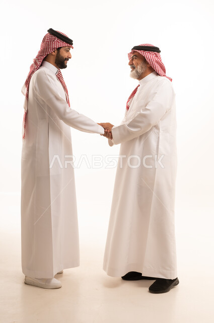 Expressions of appreciation and respect for elders, adherence to customs and traditions, the concept of family ties and kinship, a refined family atmosphere, a portrait of a young Saudi Arabian Gulf man wearing traditional thobe and shemagh kissing his father, gestures of greeting and peace, full body, white background