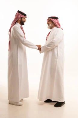 تعابير التقدير واحترام كبار السن, التمسك بالعادات والتقاليد, مفهوم الترابط الأسري وصلة الرحم, أجواء عائلية راقية, بورتريه لشاب عربي خليجي سعودي يرتدي الثوب التقليدي والشماغ يقوم بتقبيل بمصاحة والده, ايماءات إلقاء التحية والسلام, الجسم بالطول الكامل, خلفية بيضاء