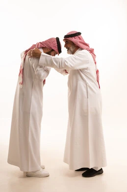 تعابير التقدير واحترام كبار السن, التمسك بالعادات والتقاليد, مفهوم الترابط الأسري وصلة الرحم, أجواء عائلية راقية, بورتريه لشاب عربي خليجي سعودي يرتدي الثوب التقليدي والشماغ يقوم بتقبيل يد والده, ايماءات إلقاء التحية والسلام, الجسم بالطول الكامل, خلفية بيضاء