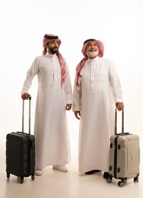 Having a good time on vacation with family, enjoying travel and summer trips, portrait of an elderly Saudi Arabian Gulf man wearing traditional thobe and shemagh holding a suitcase standing next to his son, gestures of joy and happiness, full body photo, white background