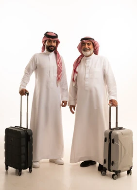 قضاء أوقات ممتعة في الإجازة برفقة العائلة, الاستمتاع بالسفر و الرحلات الصيفية, بورتريه لرجل عربي خليجي سعودي كبير في السن يرتدي الثوب التقليدي والشماغ يمسك بيده حقيبة السفر يقف بجانب ابنه, إيماءات الفرح و السرور, صورة للجسم بالطول الكامل, خلفية بيضاء