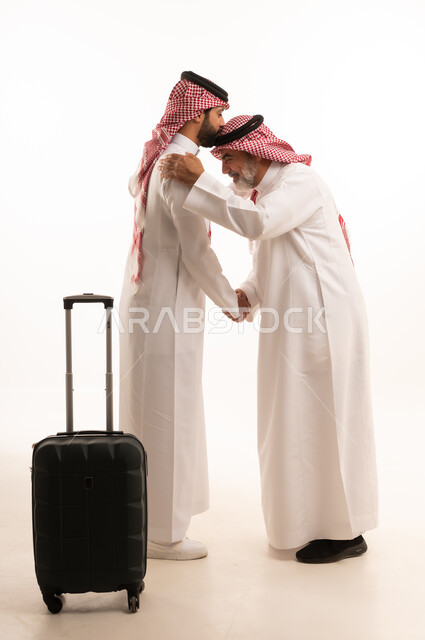 الاستقبال والتوديع عند السفر, القاء التحية والسلام, قضاء أوقات ممتعة في الإجازة برفقة العائلة, بورتريه لرجل عربي خليجي سعودي كبير في السن يرتدي الثوب التقليدي والشماغ يمسك بيده حقيبة السفر يقف بجانب ابنه, صورة للجسم بالطول الكامل, خلفية بيضاء