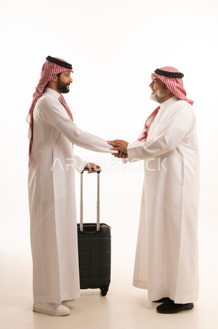 الاستقبال والتوديع عند السفر, القاء التحية والسلام, قضاء أوقات ممتعة في الإجازة برفقة العائلة, بورتريه لرجل عربي خليجي سعودي كبير في السن يرتدي الثوب التقليدي والشماغ يمسك بيده حقيبة السفر يقف بجانب ابنه, صورة للجسم بالطول الكامل, خلفية بيضاء