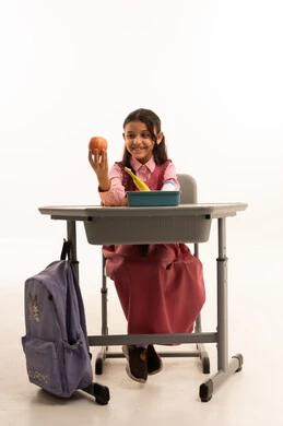  تناول وجبة الفطور الصحية في الفسحة المدرسية، الاستمتاع بتناول الأطعمة الصحية في وقت الفسحة المدرسية، موسم العودة للمدارس، بورتريه لطالبة عربيه خليجيه سعودية ترتدي الزي المدرسة تجلس على الطاوله المكتبية، خلفية بيضاء